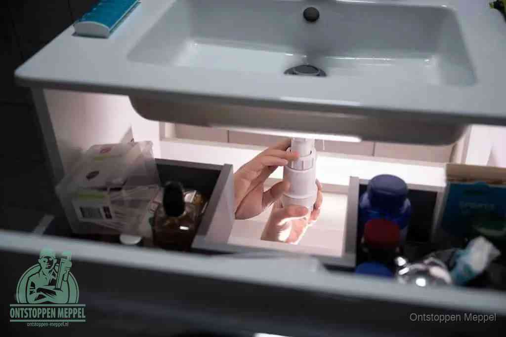 Een pompfles met zeep boven een wastafel, de heet water en afwasmiddel-methode om een vetprop in de afvoer los te maken in Meppel