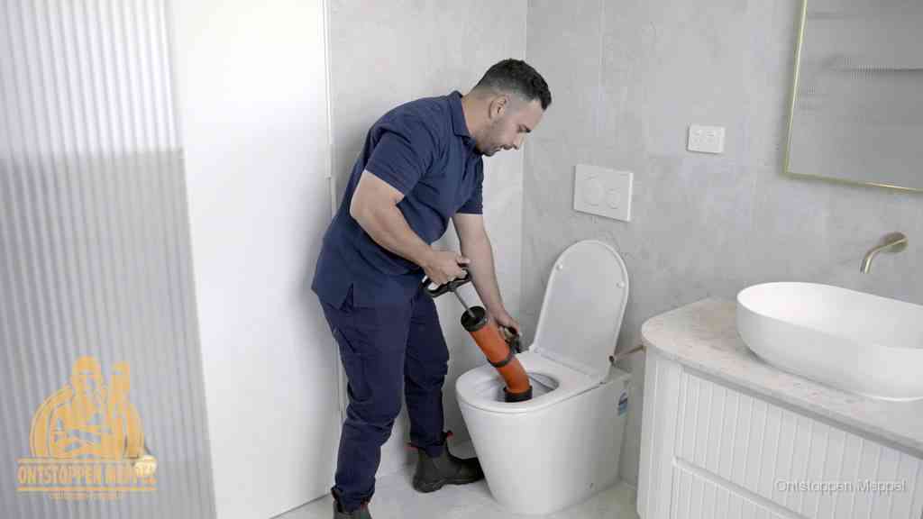 Een monteur buigt over een wandcloset en duwt met de hand een persluchtontstopper in de toiletpot om de verstopping handmatig los te maken in Meppel Een monteur buigt over een wandcloset en duwt met de hand een persluchtontstopper in de toiletpot om de verstopping handmatig los te maken in Meppel