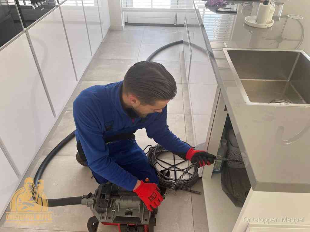 Een monteur ontstopt de keukenafvoer onder de spoelbak met een elektrische veermachine in Meppel