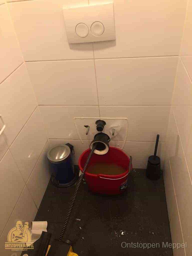 Een ontstopte wand-wc met verwijderde toiletpot waar een ontstoppingsveer in de wanduitgang verdwijnt, het achterhalen waar de verstopping zit in Meppel Een ontstopte wand-wc met verwijderde toiletpot waar een ontstoppingsveer in de wanduitgang verdwijnt, het achterhalen waar de verstopping zit in Meppel
