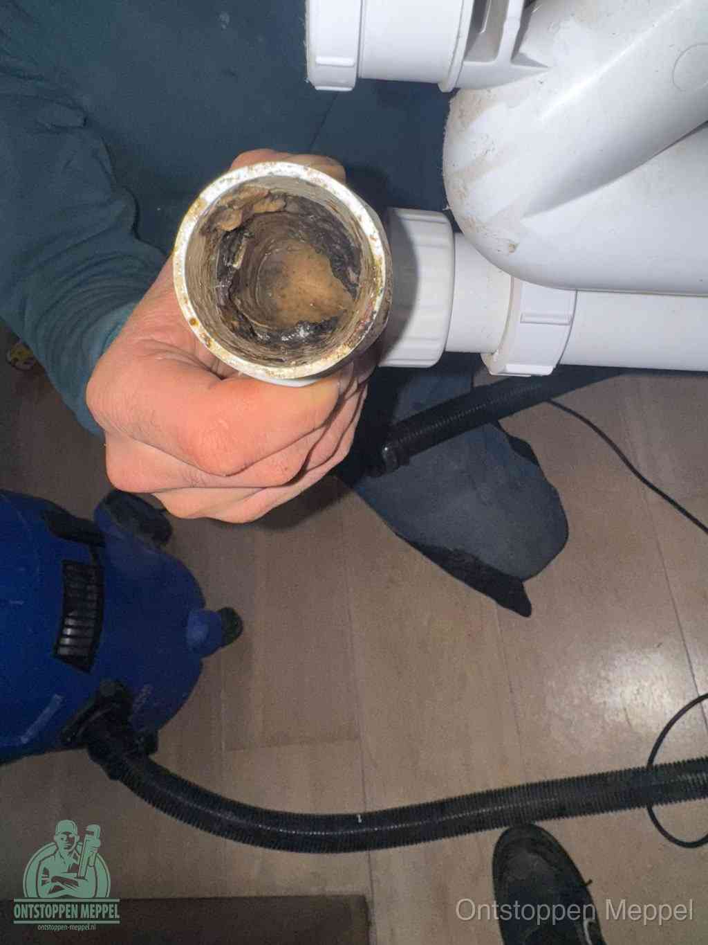 Een hand houdt een losgekoppeld PVC-afvoerbuisstuk vast dat van binnen volledig is dichtgeslibd met vet, vuil en aanslag, de meest voorkomende oorzaak van een verstopte afvoer in Meppel