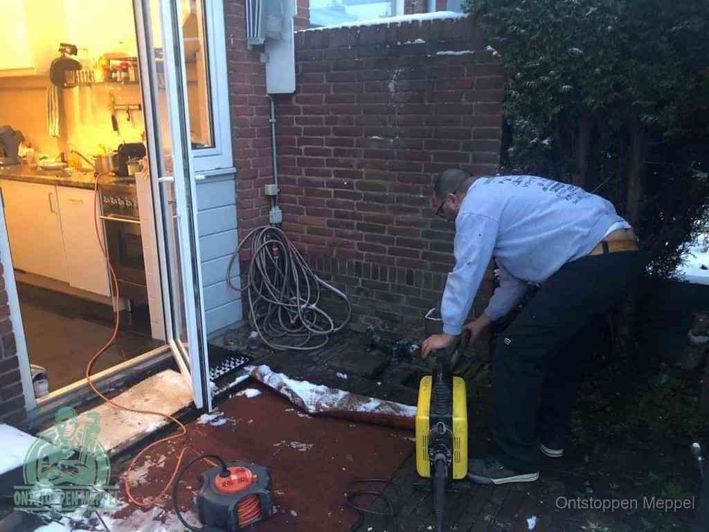 Een monteur werkt buiten bij een open riool-/grondput met een elektrische ontstoppingsmachine om een verborgen afvoerprobleem op te sporen in Meppel