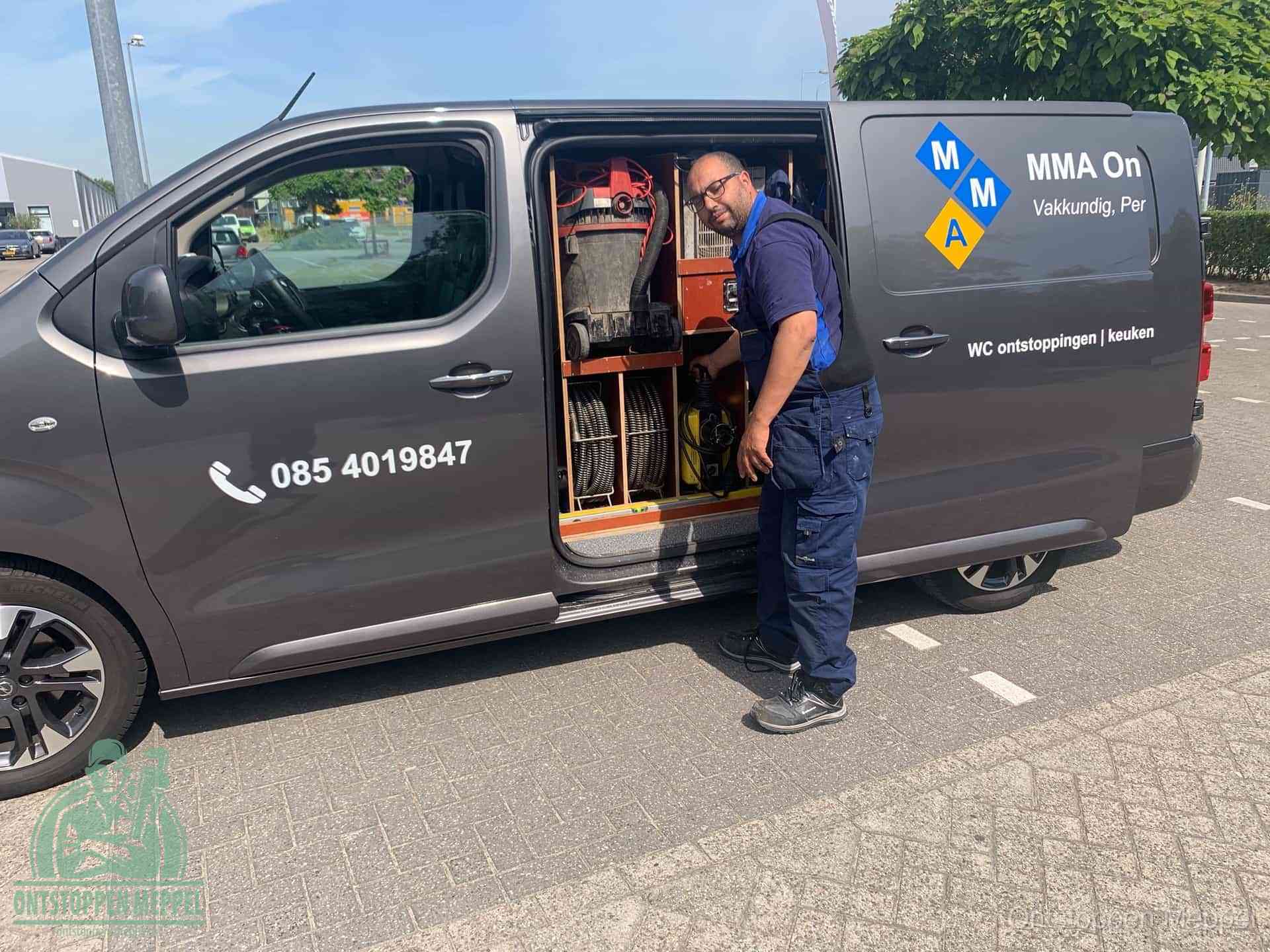 Een monteur bij de open schuifdeur van zijn bedrijfsbus op een parkeerplaats, klaar om de oorzaak van terugkerende afvoerverstoppingen aan te pakken in Meppel