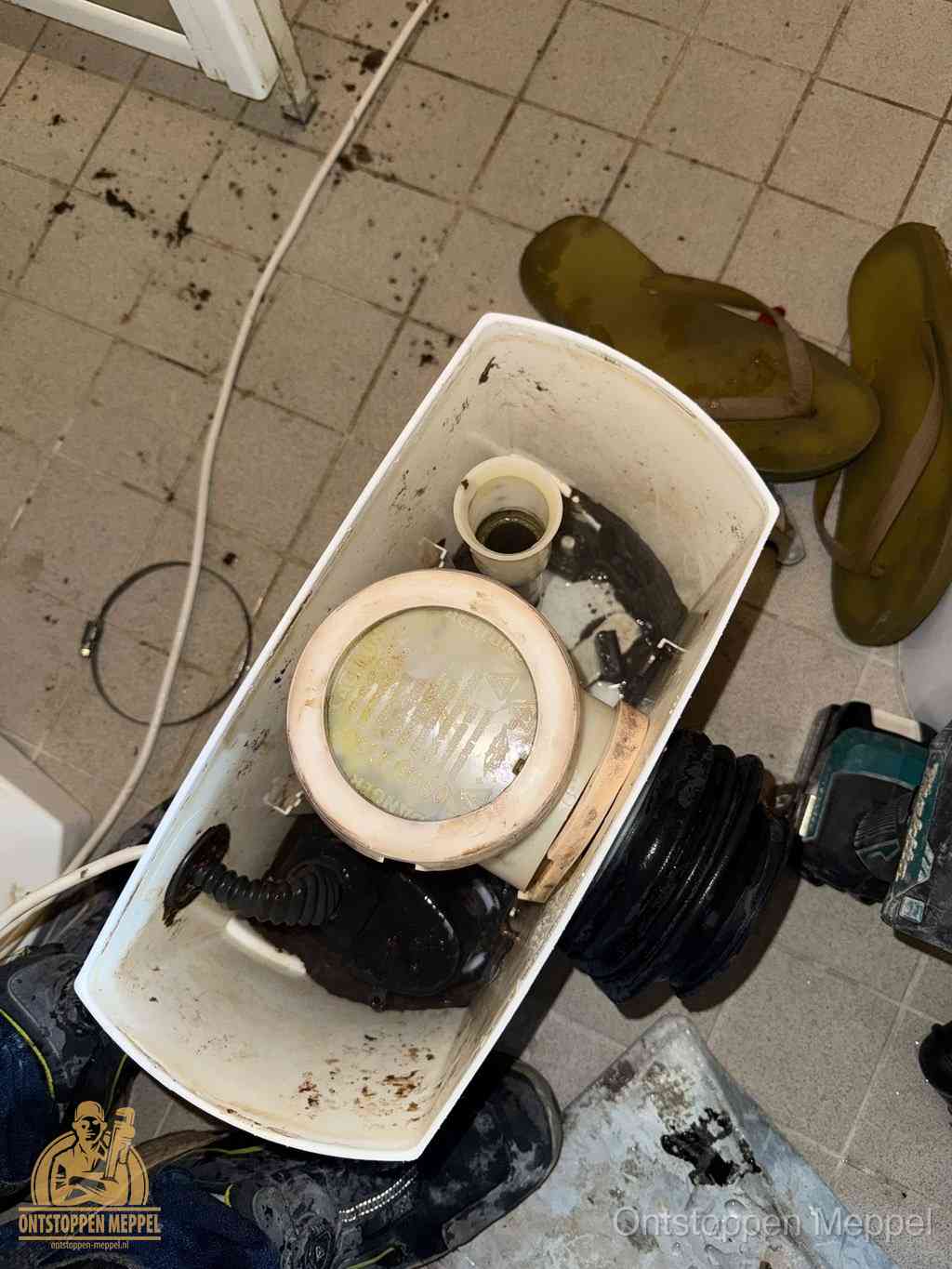 Een gedemonteerde toiletpot op de vloer met ontstoppingsveer en gereedschap ernaast, het verwijderen van een vastzittend voorwerp uit de wc in Meppel Een gedemonteerde toiletpot op de vloer met ontstoppingsveer en gereedschap ernaast, het verwijderen van een vastzittend voorwerp uit de wc in Meppel