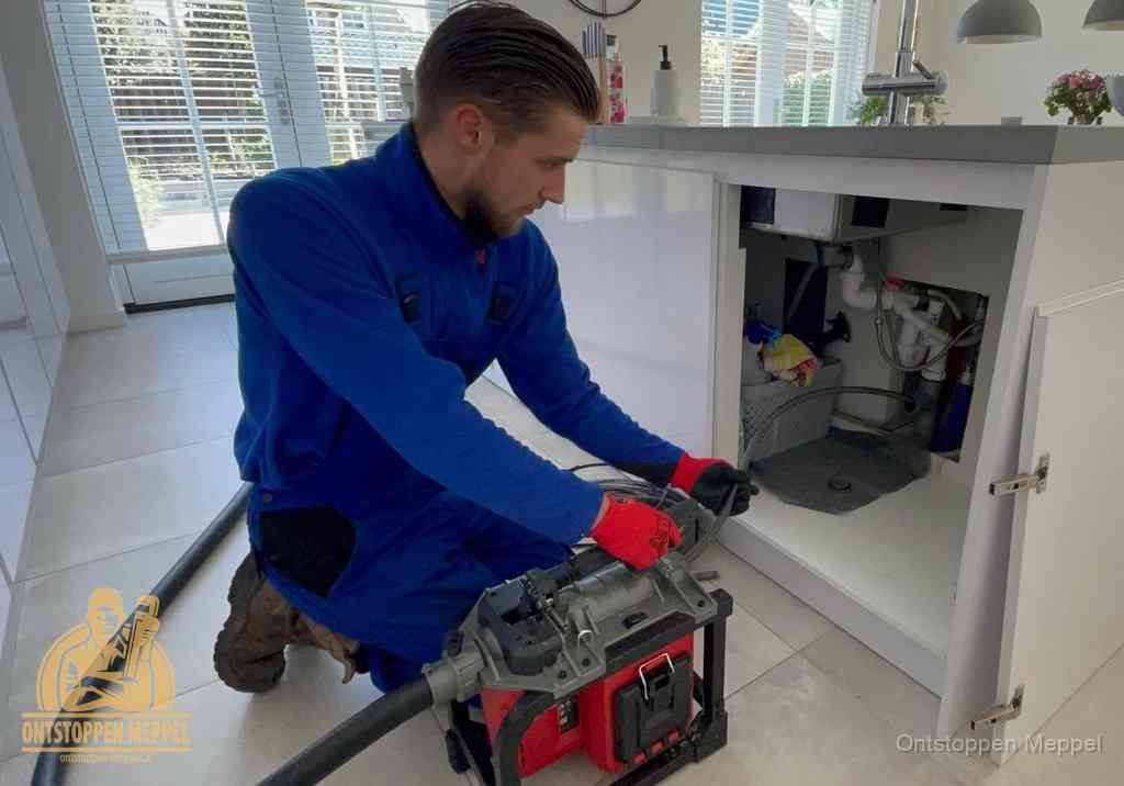 Een monteur voert een professionele elektrische ontstoppingsmachine in de afvoer onder de spoelbak tijdens het gootsteen ontstoppen in Meppel